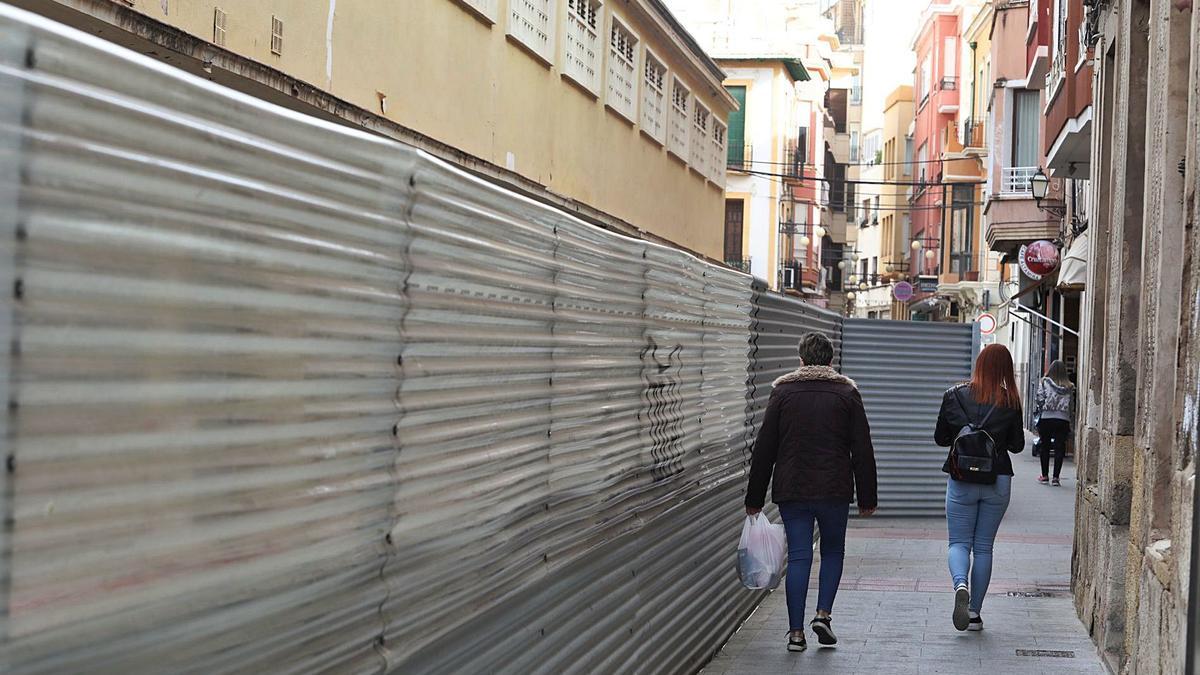 Tres mujeres caminan junto a las vallas que rodean el Mercado Central de Elche, cuyo proyecto pretende romper el Ayuntamiento.