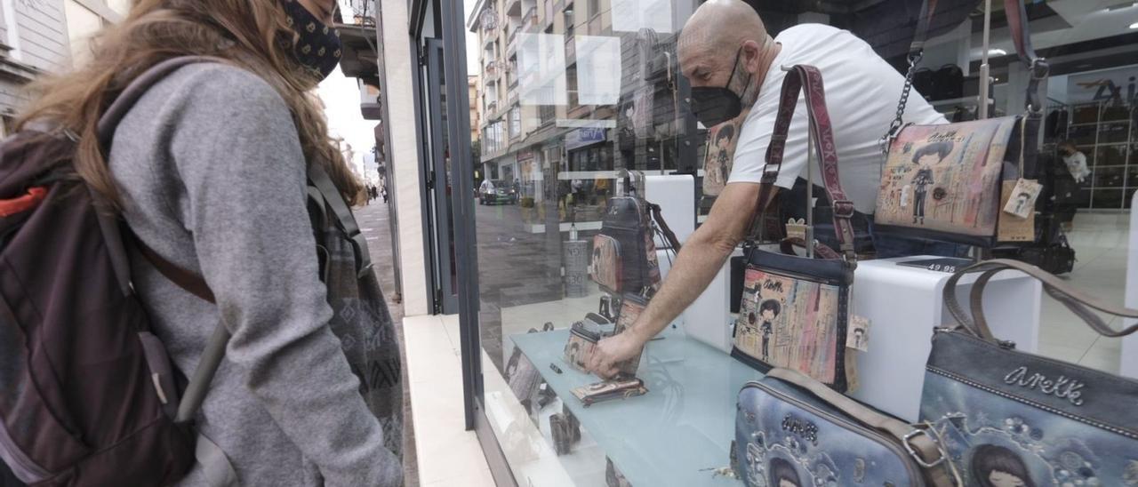 Una mujer observa un escaparate de una céntrica calle de La Laguna mientras un comerciante coge un artículo.