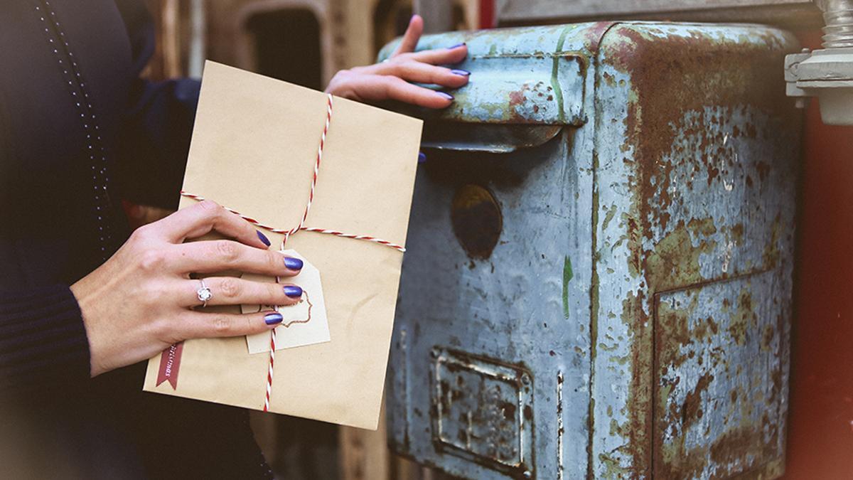 Una mujer echa una carta a un buzón.