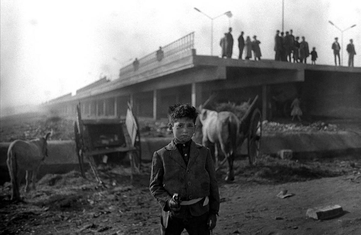 Un chico empuña una pistola de juguete en el Somorrostro, en 1964, con el paseo Marítimo de la Barceloneta detrás.