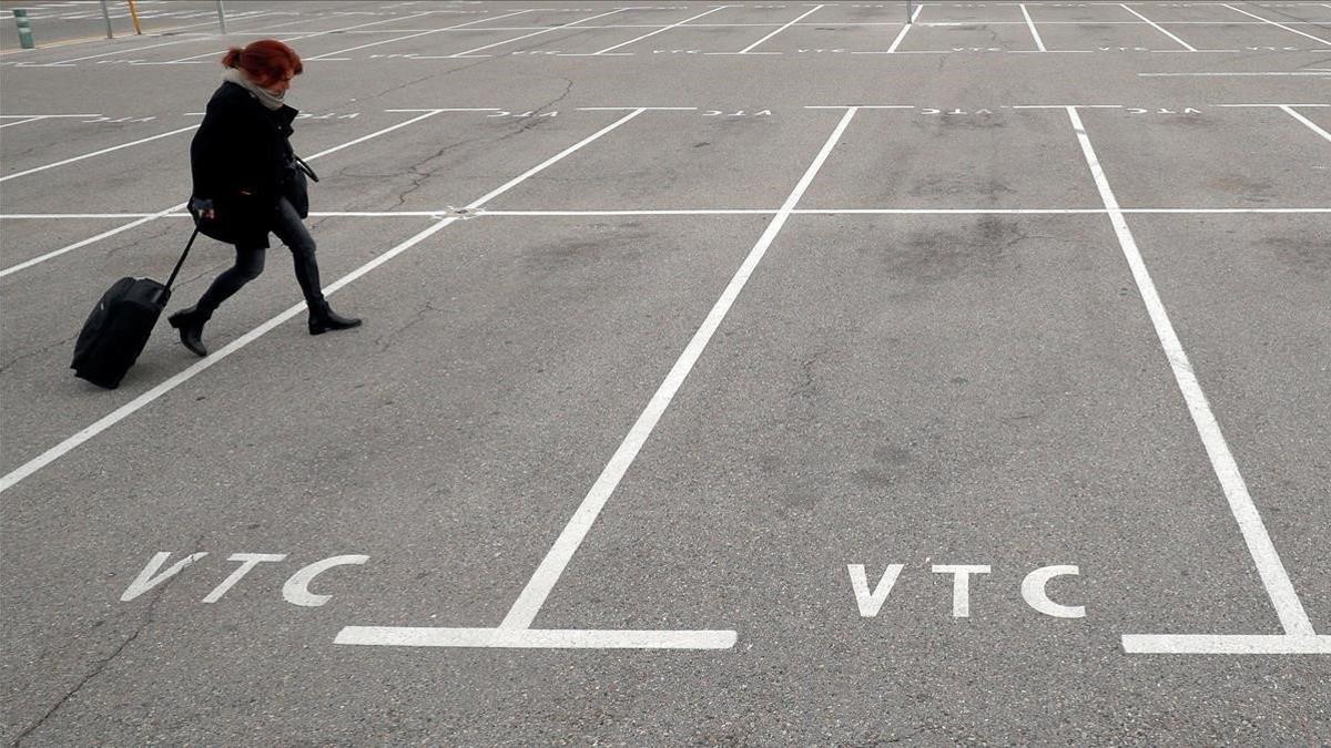 Una mujer pasa por los estacionamientos vacíos asignados para los VTC en el aeropuerto del Prat.