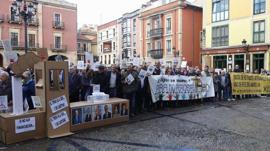 Manifestantes en la plaza Mayor de Gijón, con pancartas, proclamas y un tren de cartón.
