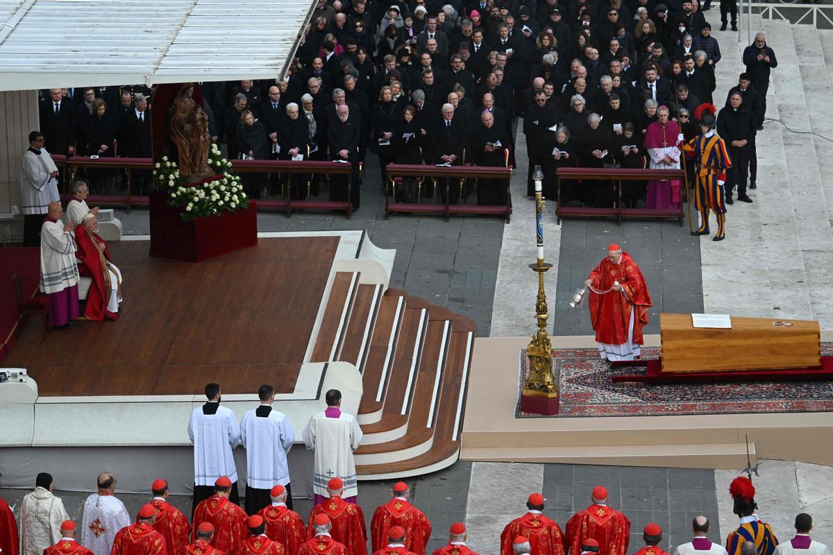El cardenal italiano Giovanni Battista Re (derecha) bendice el ataúd del papa emérito Benedicto XVI, mientras el papa Francisco observa (arriba a la izquierda) durante su misa fúnebre en la plaza de San Pedro.
