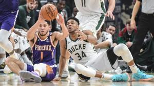 Devin Booker y Antetokounmpo pelean desde el suelo por un balón.