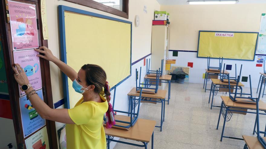 Una profesora coloca carteles de medidas preventivas ante el COVID-19 en el aula antes del inicio del curso.