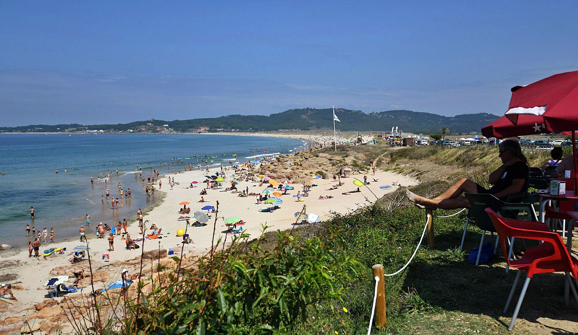 La playa de A Lanzada, en O Grove, con bañistas en la arena y una persona en un chiringuito. 