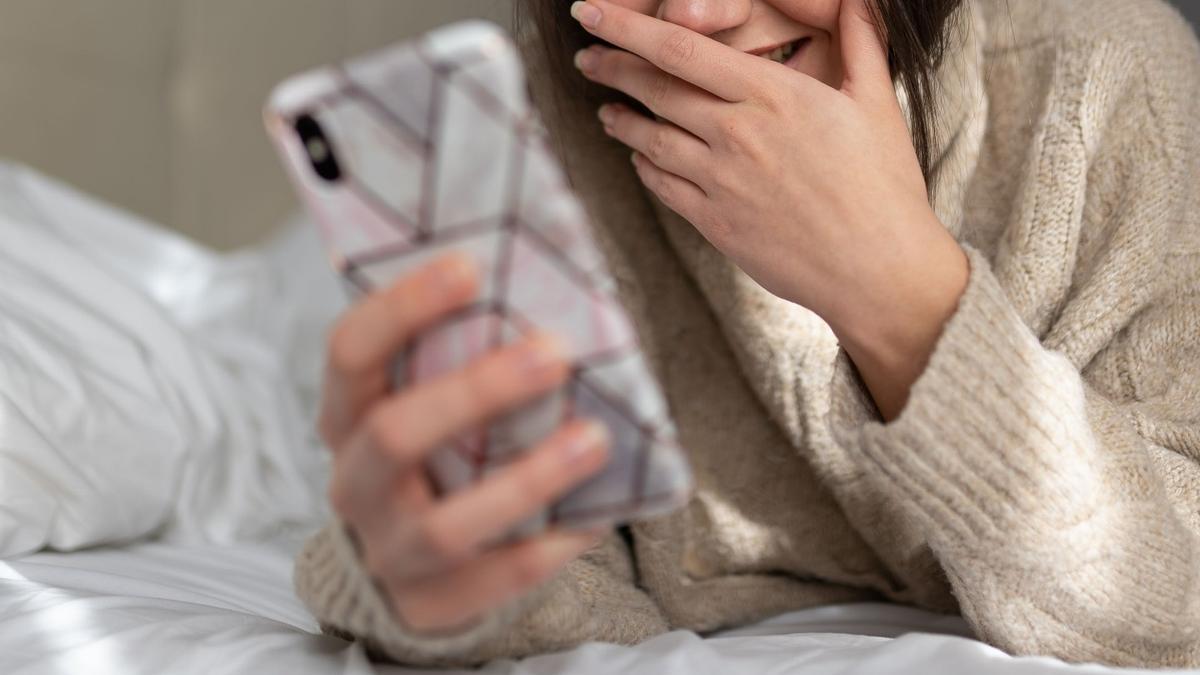 Una joven se ríe mientras usa su teléfono móvil