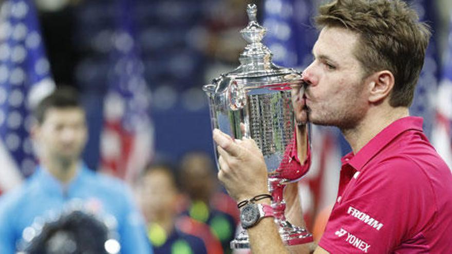 Wawrinka levanta su título de campeón, con Djokovic de fondo.