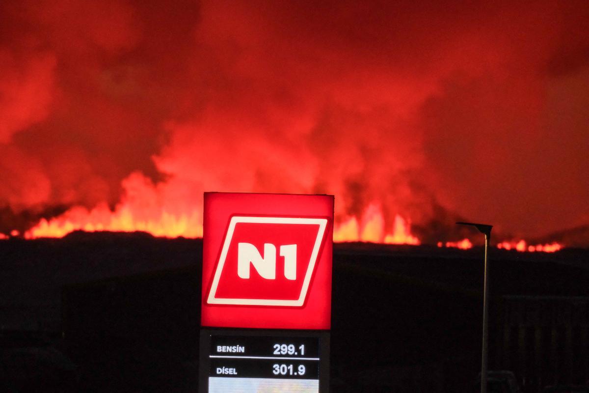 El logotipo de una gasolinera se ve mientras lava y nubes de humo salen de una fisura durante una erupción volcánica cerca de Grindavik, en el oeste de Islandia, el 8 de febrero de 2023.