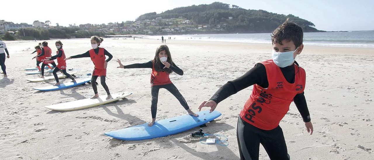 Dos grupos en plena clase de surf con sus monitores, de blanco, en plena clase.