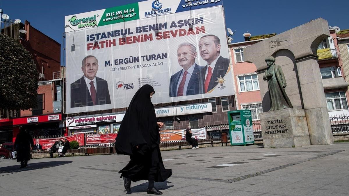 Una mujer camina frente a un cartel electoral que muestra al presidente turno, Recep Tayyip Erdogan, y al candidato de su partido, el AKP, para la alcaldía de Estambul. Binali Yildirim.