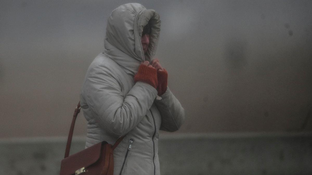 Una mujer se abriga del frío, el viento y la lluvia en València este sábado.