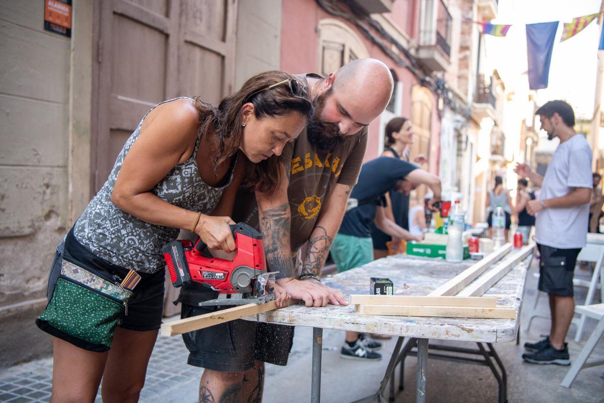 Vecinos de la calle Congrés cortando listones de madera durante la creación de ‘guarnits’ para las fiestas mayores de Gràcia. Barcelona, 4 de agosto de 2026. Foto: Belén González / EP