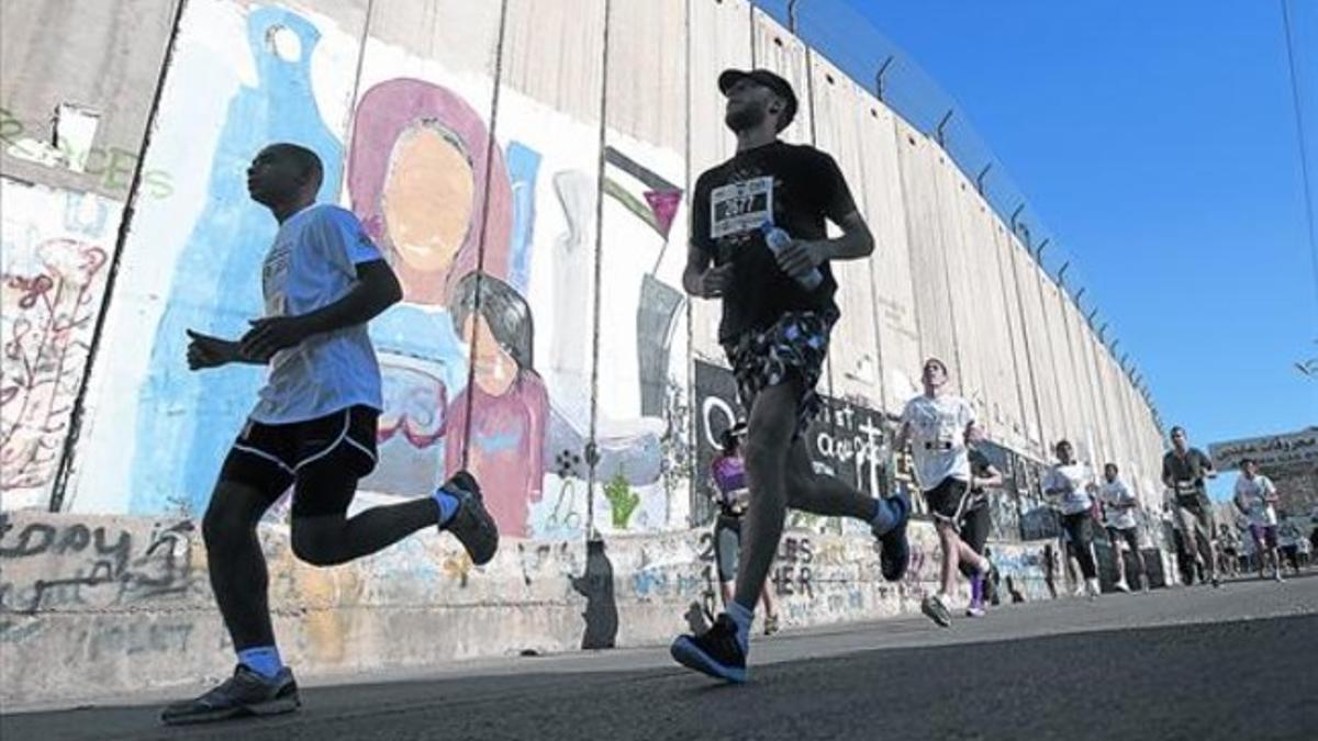 En plena carrera 8 Corredores del maratón pasan junto al muro levantado por el Gobierno israelí en Belén.