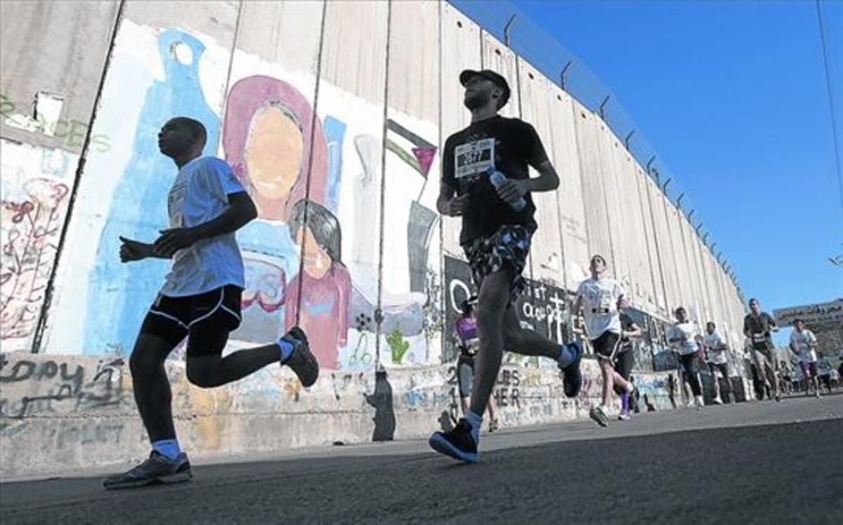 En plena carrera 8 Corredores del maratón pasan junto al muro levantado por el Gobierno israelí en Belén.