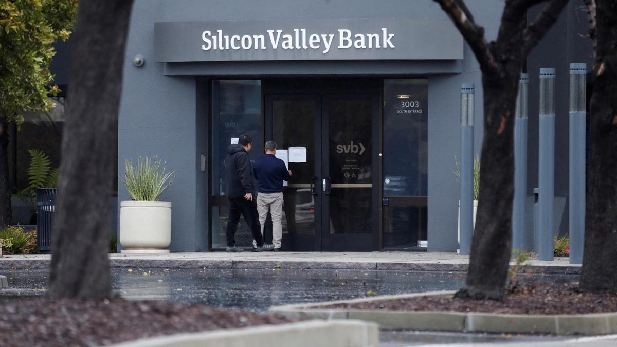 Un hombre pone un letrero en la puerta del Silicon Valley Bank mientras un espectador observa la sede del banco en Santa Clara, California.