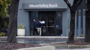 Un hombre pone un letrero en la puerta del Silicon Valley Bank mientras un espectador observa la sede del banco en Santa Clara, California.