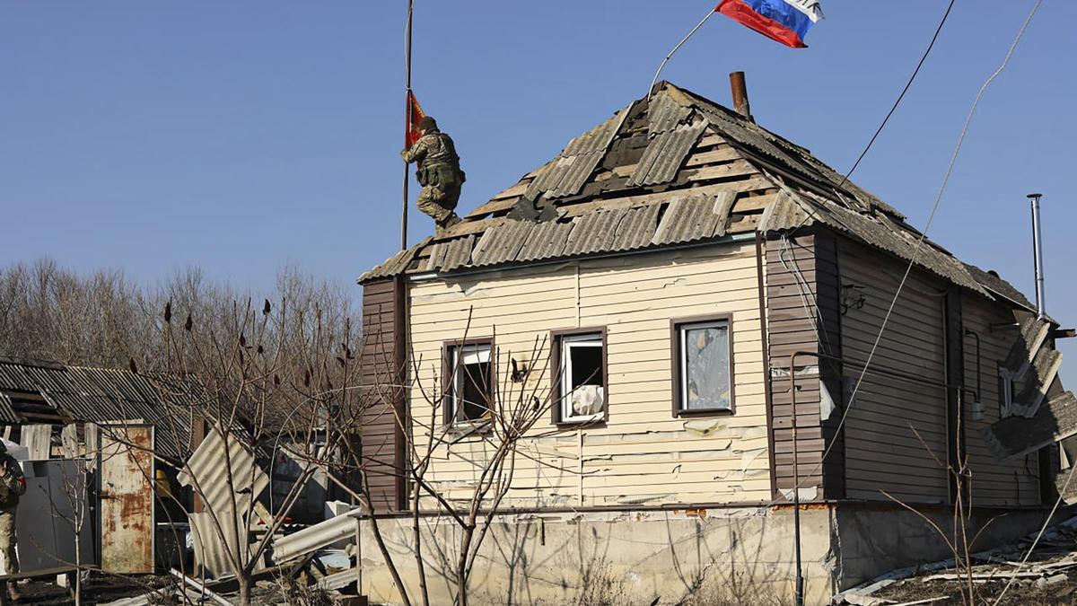 Un soldado ruso instalando una bandera roja en el techo de un edificio en un pueblo de la región de Kursk