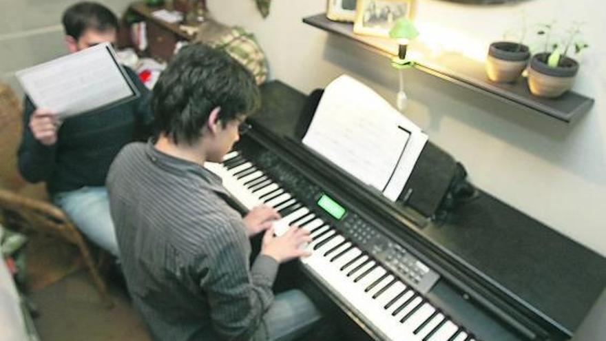 Fernando, a la izquierda, con el niño que cuida tocando el piano en su casa de Santiago. / xoán álvarez