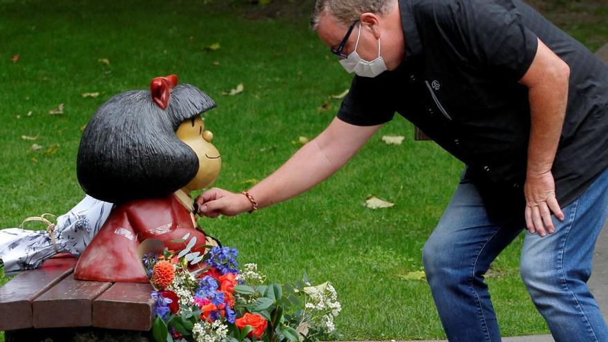 Un hombre pone flores junto a la imagen de Mafalda en honor a Quino.