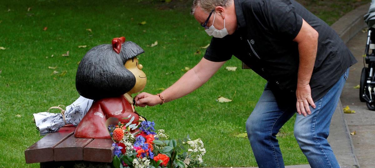 Un hombre pone flores junto a la imagen de Mafalda en honor a Quino.
