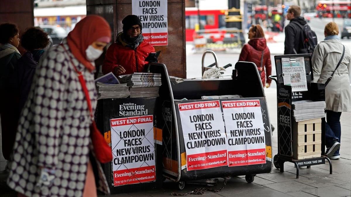 Una mujer protegida con máscara pasa junto a un kiosco que exhibe portadas sobre el impacto del coronavirus, en Londres.