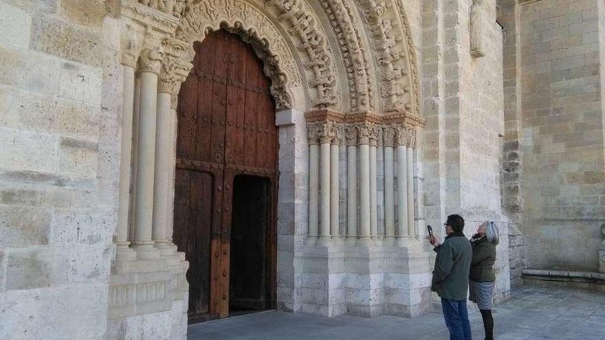 Dos turistas utilizan las nuevas audiogías para conocer la historia de la portada norte de la Colegiata.