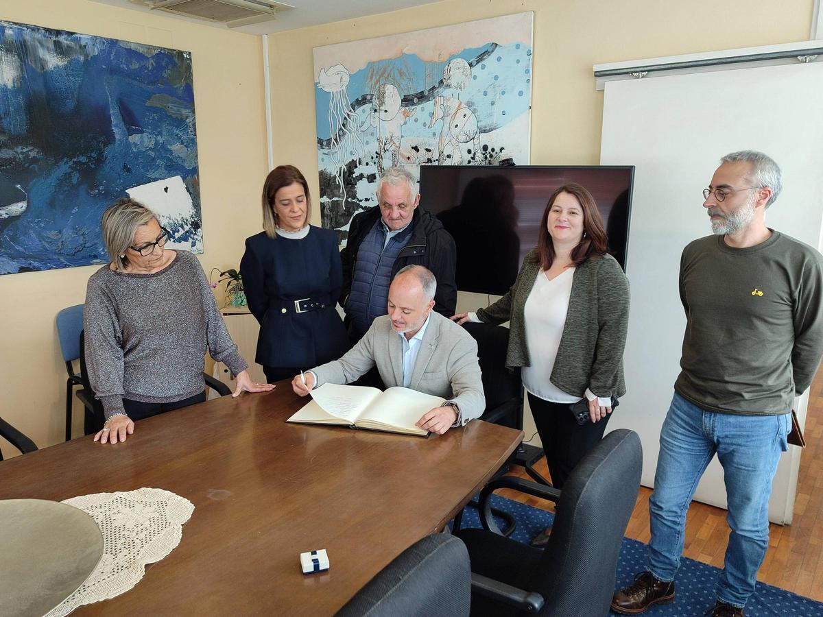 David Regades firmando en el libro de honor del Concello y detrás el gobierno municipal.