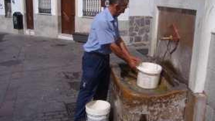 Un hombre llena un cubo de agua de una fuente de Yunquera.