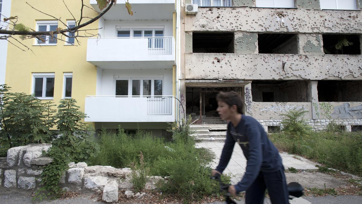 Un chico pasa en bicicleta frente a edificios nuevos y edificios con marcas de la guerra en Bosnia en el año 2013.