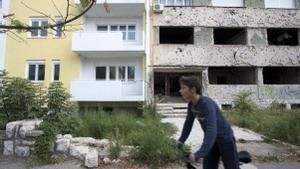 Un chico pasa en bicicleta frente a edificios nuevos y edificios con marcas de la guerra en Bosnia en el año 2013. 