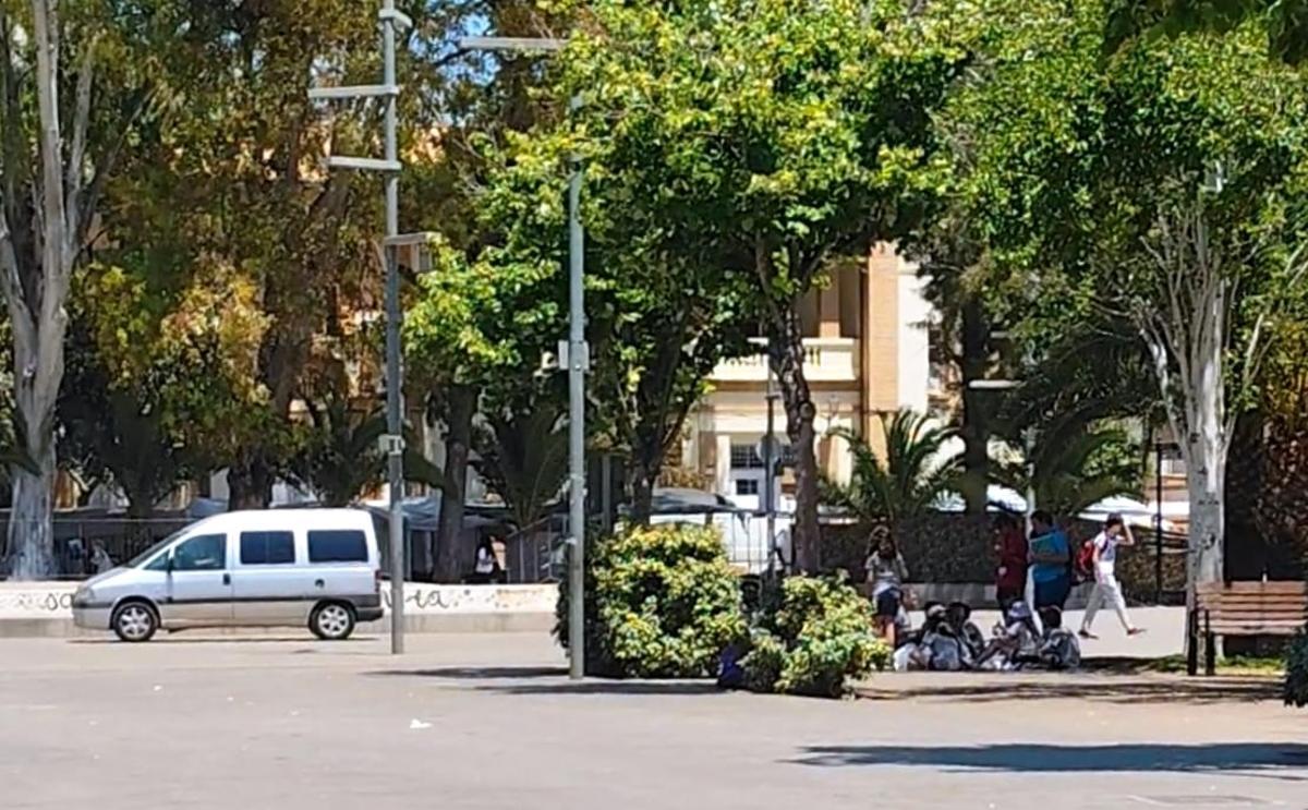 Un vehículo en la plaza próximo a un grupo de estudiantes.