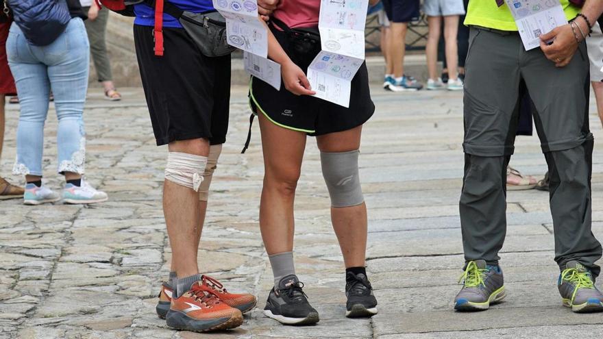 Tres peregrinos, dos de ellos con vendajes en la rodilla, muestran sus credenciales del Camino