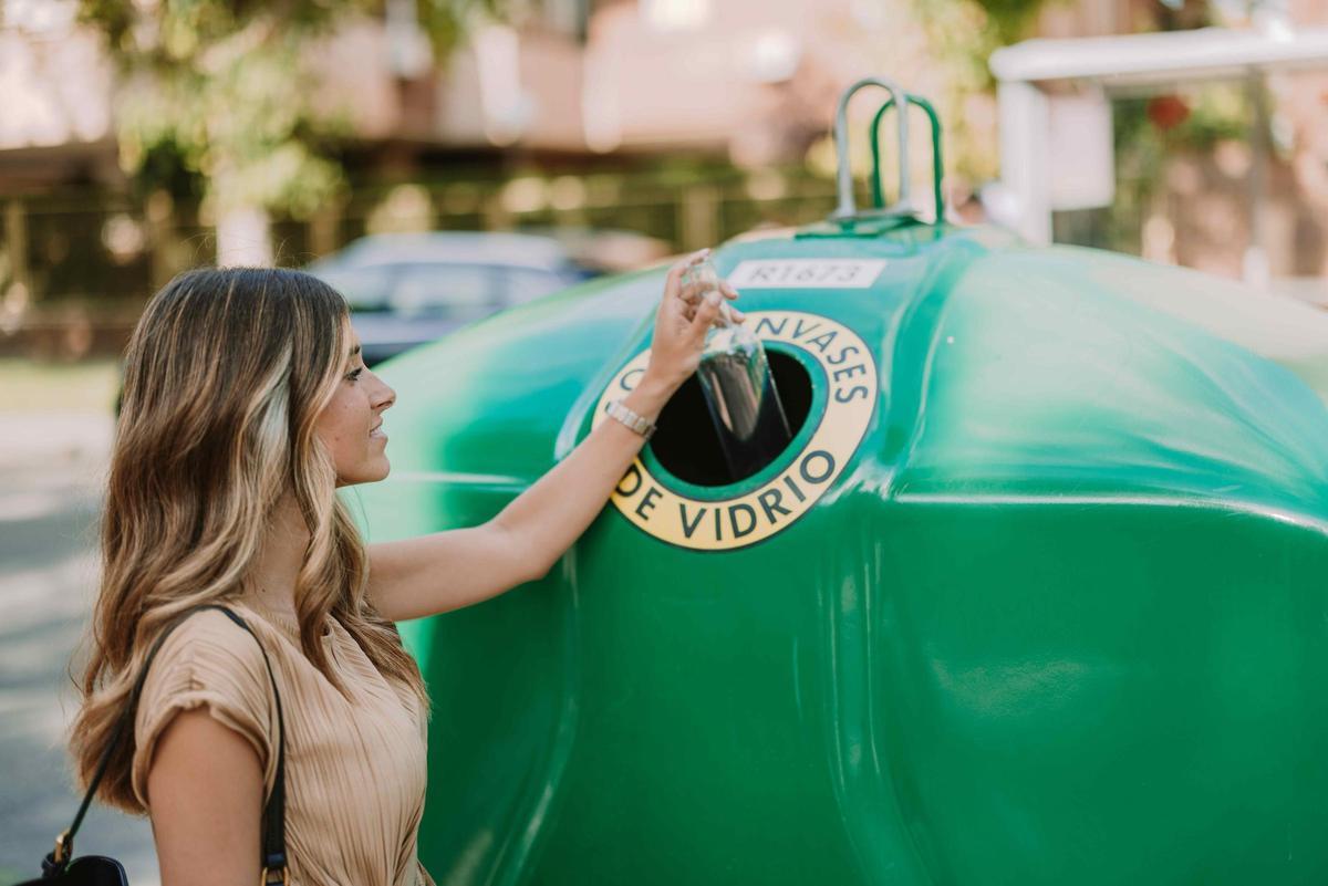 Una joven deposita una botella en un contenedor de vidrio.