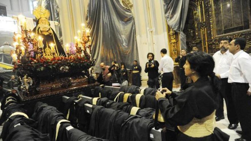 Una hermana de la Santa Cruz le reza a la Virgen de los Dolores en su Amparo, con los varales del trono llenos ya de las túnicas de los portadores.