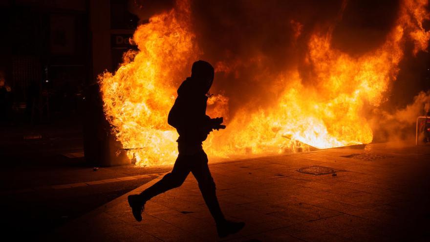 Un manifestante corre ante contenedores incendiados en los disturbios en la manifestación en apoyo a Hasel en Barcelona
