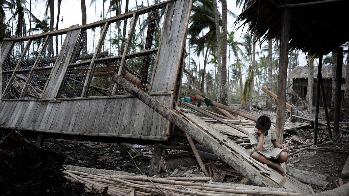 Un niño lee sobre una casa en ruinas en mayo de 2008, tras el paso de un huracán, en Birmania.