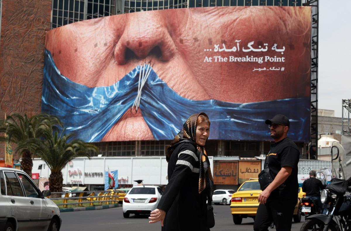 Unos iraníes pasan junto a una enorme valla publicitaria contra Estados Unidos en la que se hace referencia al presidente estadounidense Donald Trump y al estrecho de Ormuz, en la plaza Valiasr de Teherán (Irán), el 2 de mayo de 2026.