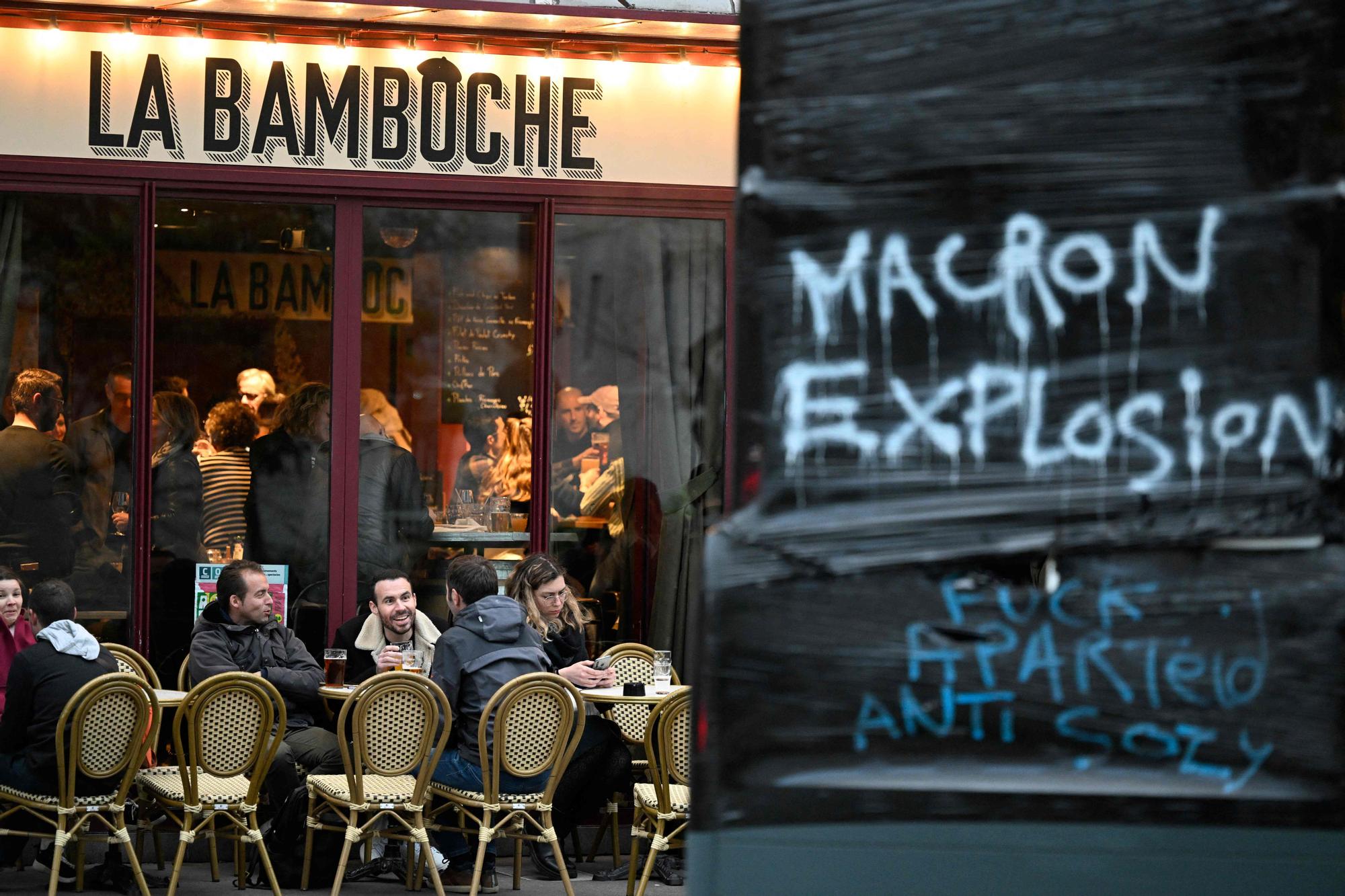 Una terraza de un bar de París junto a una pintada en la que se puede leer &quot;Macron explosión&quot;, este sábado, un día después de que el Consejo Constitucional diera su aval a la reforma de las pensiones.