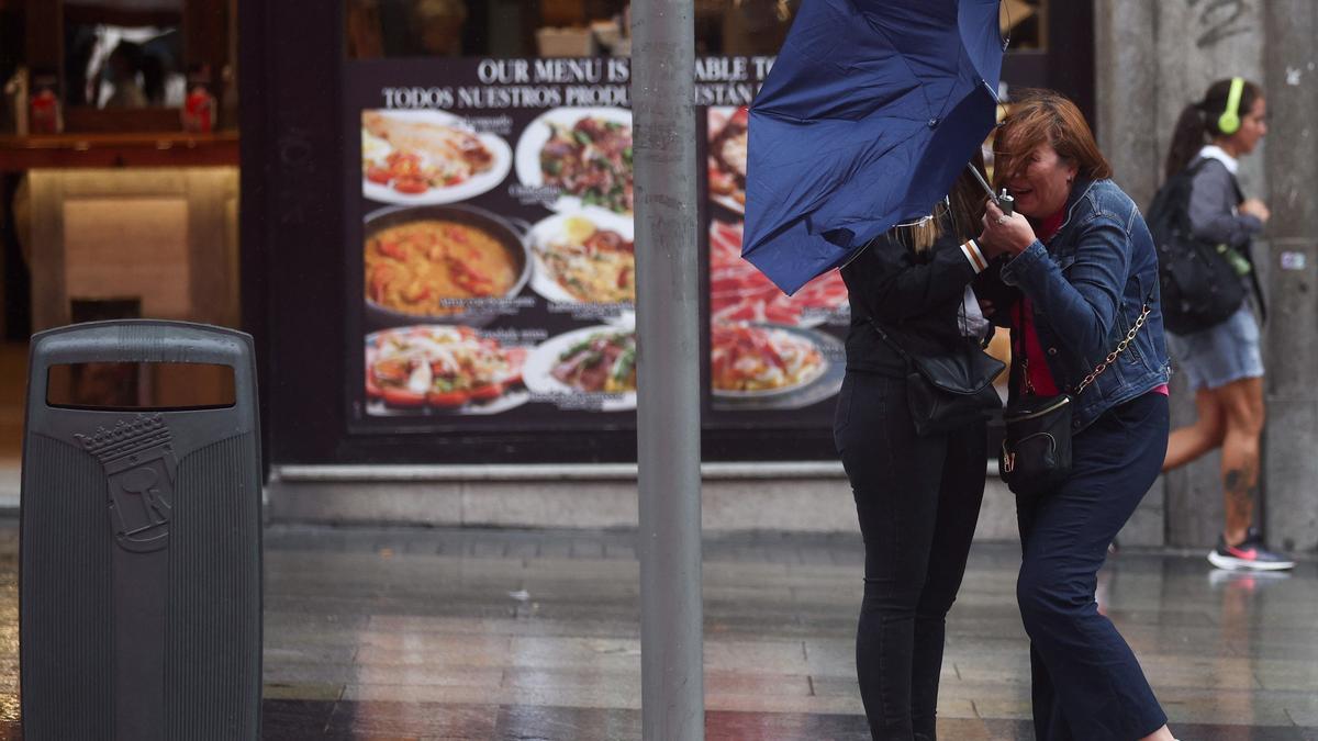 Dos chicas intentan controlar su paraguas, en la calle Gran Vía de Madrid.