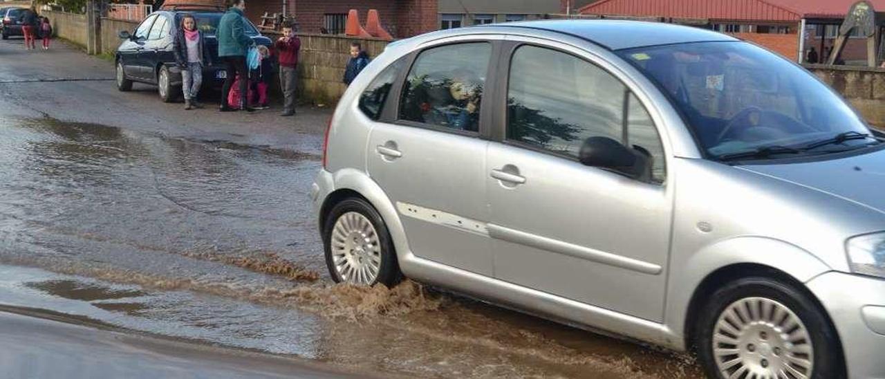 Un coche pasa ayer por el charco de mayor tamaño, a pocos metros de la entrada del colegio.