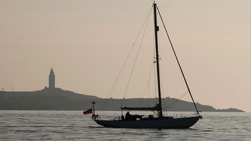 Una embarcación navega en A Coruña con la Torre de Hércules al fondo.