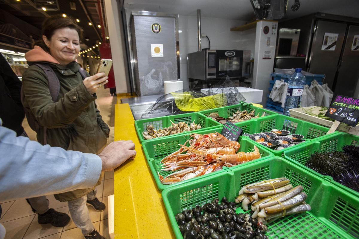 Una mujer hace una foto a las cigalas en un puesto de pescadería del Mercado Central de Alicante.