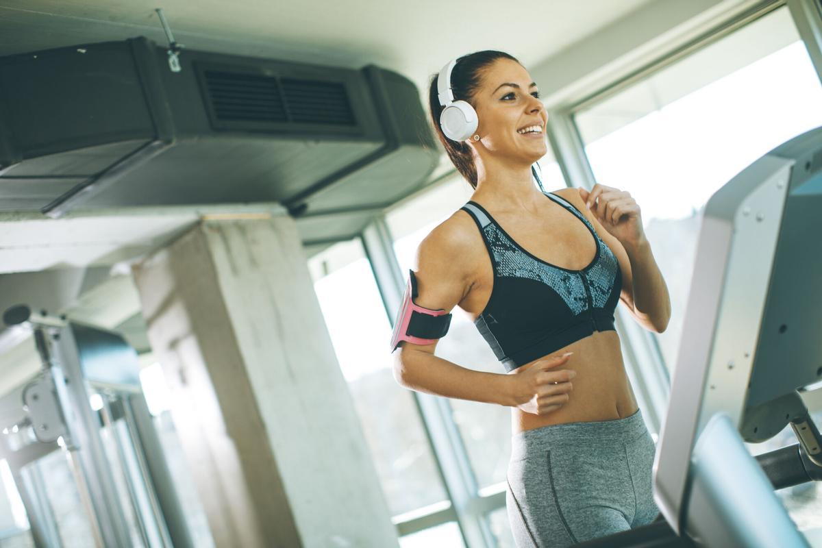 UNA MUJER JOVEN EN UNA CINTA DE CORRER DE UN GIMNASIO. Pretty young woman running on treadmill during sports training in a gym. EJERCICIO