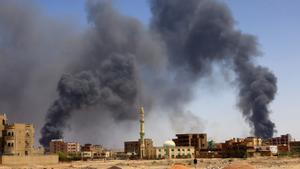 Un hombre camina con el humo al fondo tras un bombardeo aéreo en Sudán.