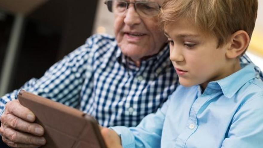 Un niño enseña a su abuelo a utilizar una tablet.