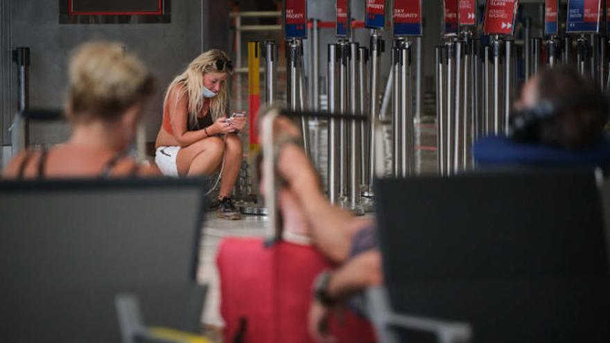 Una turista británica, con la mascarilla mal puesta, consulta su móvil en el aeropuerto de Tenerife Sur.