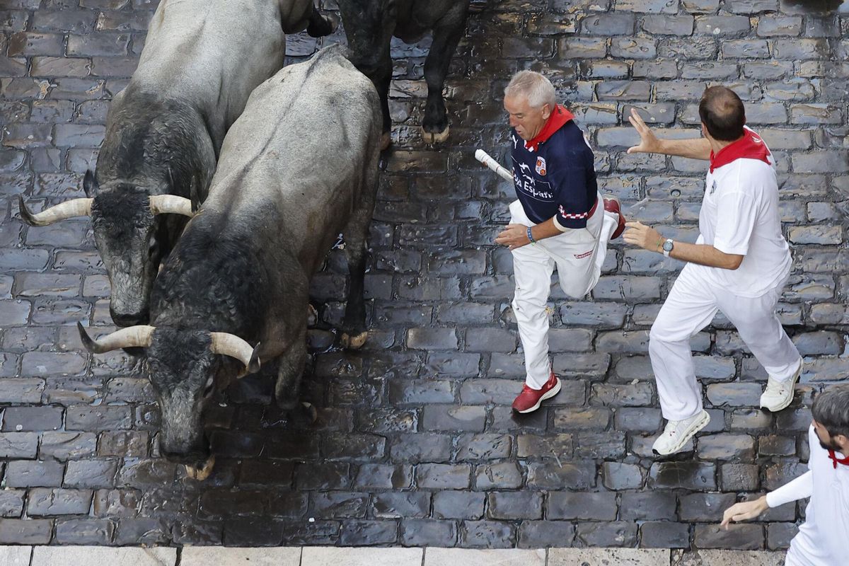 PAMPLONA, 12/07/2025.- Mozos perseguidos por los toros de la ganadería de José Escolar en el sexto encierro de los Sanfermines, este sábado en Pamplona. EFE/ Villar López
