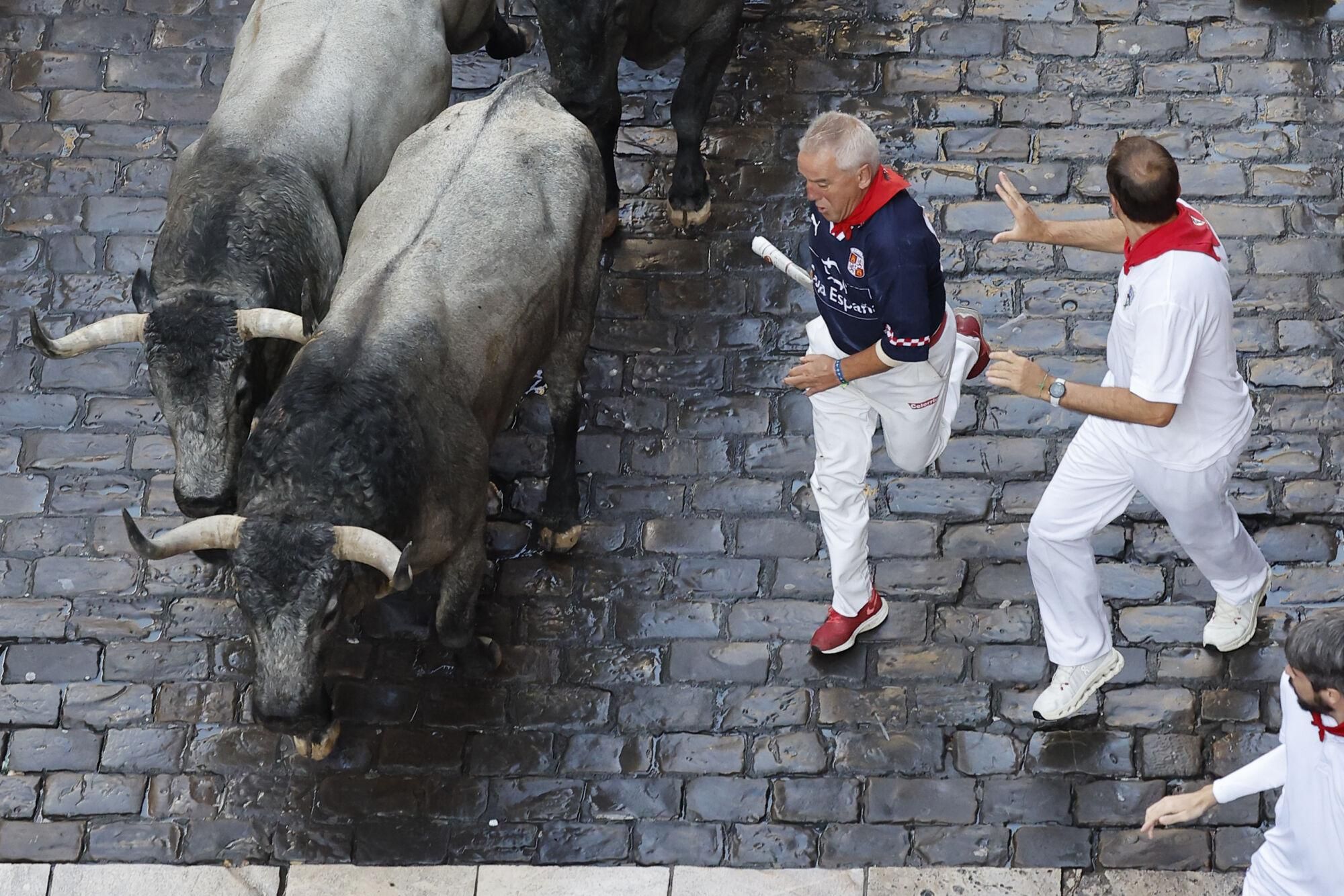 PAMPLONA, 12/07/2025.- Mozos perseguidos por los toros de la ganadería de José Escolar en el sexto encierro de los Sanfermines, este sábado en Pamplona. EFE/ Villar López