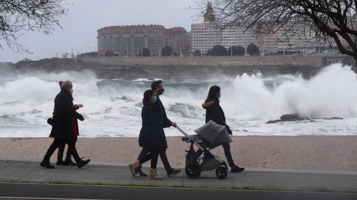 Viandantes en el paseo marítimo de A Coruña, con las olas y la torre de Hércules al fondo.   | // CARLOS PARDELLAS